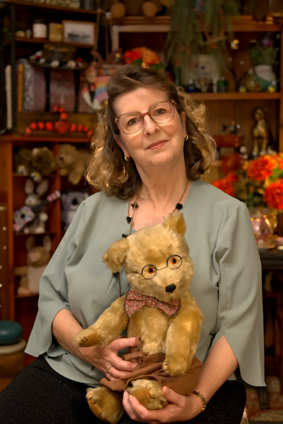 Miss Lisa holding a well-loved golden teddy bear in wire-rimmed glasses
