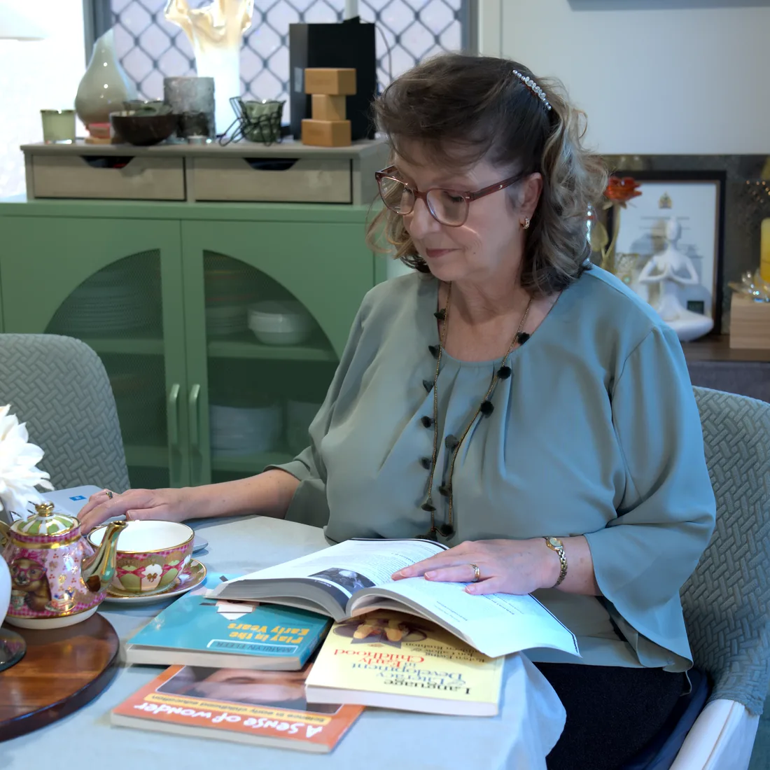 Miss Lisa reading a book on early childhood development at a table set for tea